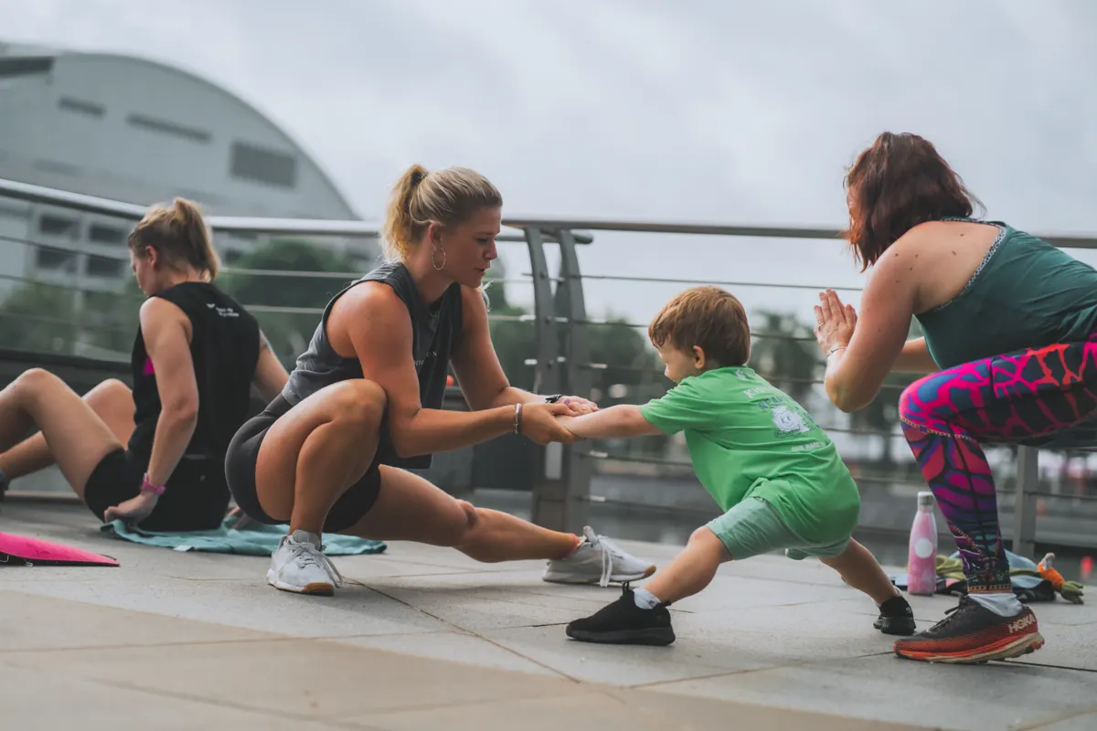 Lizzie coaching outdoors while a toddler joins in