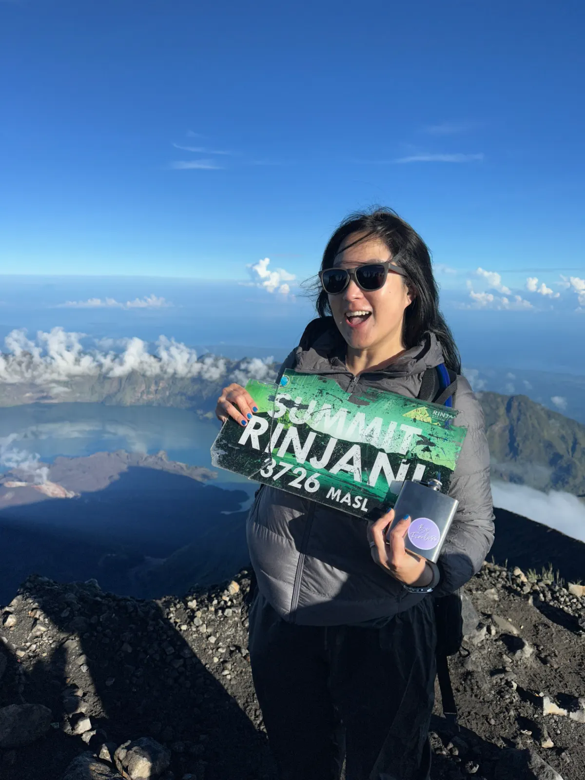 Woman holding the Rinjani summit sign above the crater lake